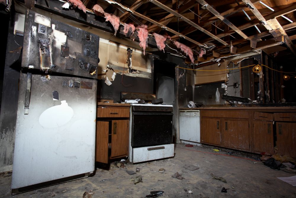 fire-damaged kitchen requiring fire restoration, showing burnt appliances, exposed insulation, and extensive smoke damage